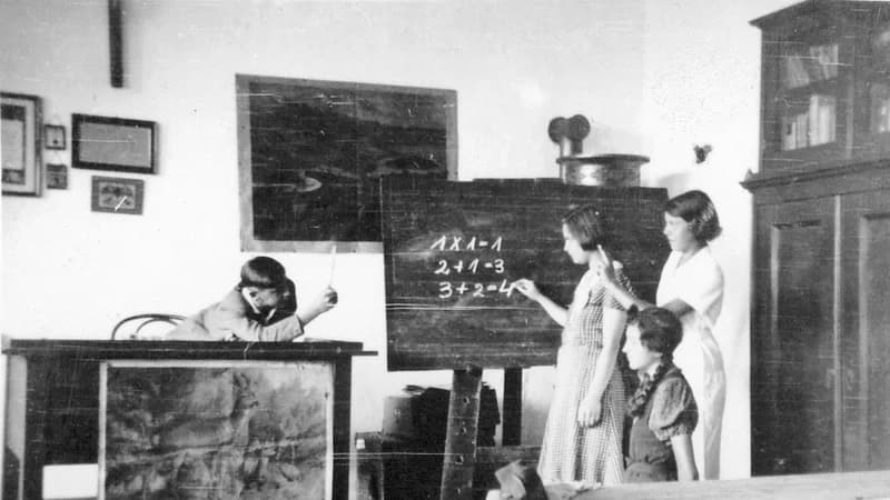 Vintage photo of a teacher and students at a classroom blackboard doing sums — learning the French futur simple